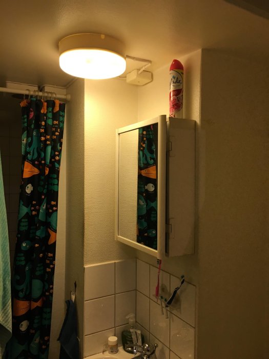 Belysning ovanför badrumsspegelskåp med öppna dörrar, vägg i behov av renovering, kaklade detaljer.