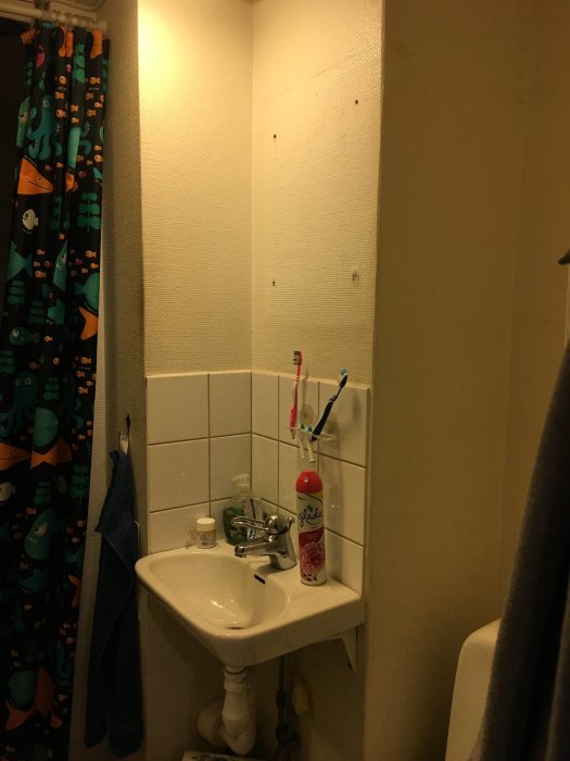 Ett orenoverat badrum med vävtapet, handfat och färgglada duschdraperier.