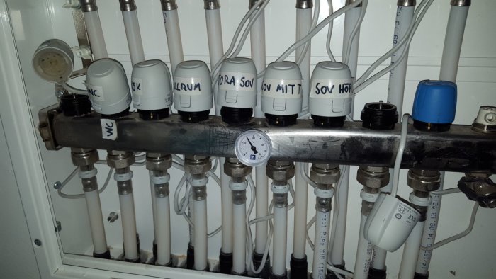 Värmefördelare med etiketterade termostatventiler och tryckmätare för uppvärmningssystem.