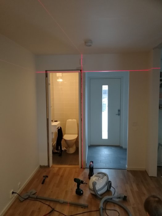 Nyinstallerad dörr i hemmiljö, med laserlinje för justering mot taket och verktyg på golvet.