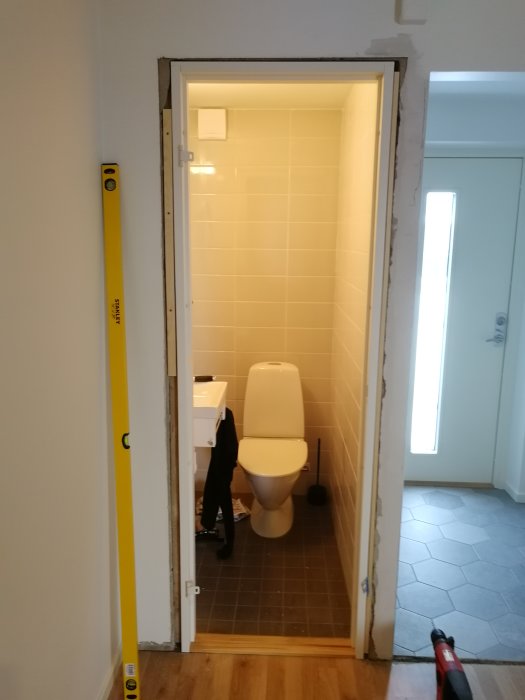 Nyinstallerad dörr linjerad med väggvalv, öppen mot ett badrum, med vattenpass och rörmokarverktyg på golvet.