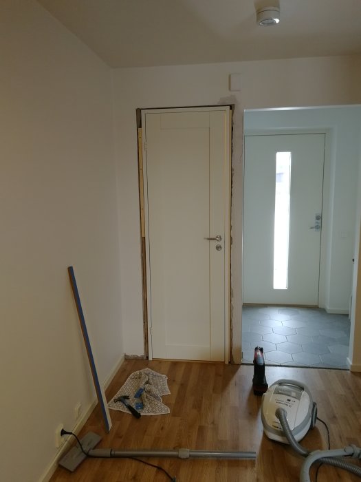 Nyinstallerad dörr med karm och dörrblad linjerad mot valvet, verktyg och städutrustning på golvet.