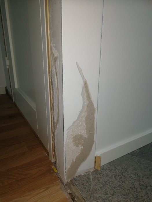 Lagad vägg med spackel på hörn intill vit dörr, golvövergång parkett till klinker.