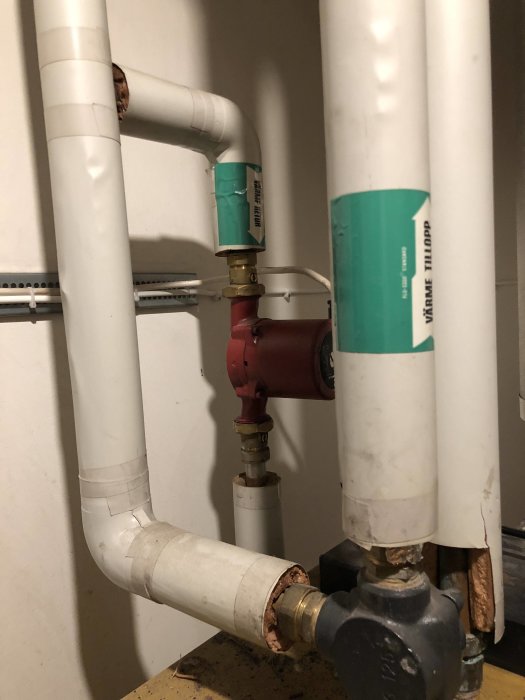 Vit VVS-rörinstallation med röd cirkulationspump och shunt i ett pannrum.