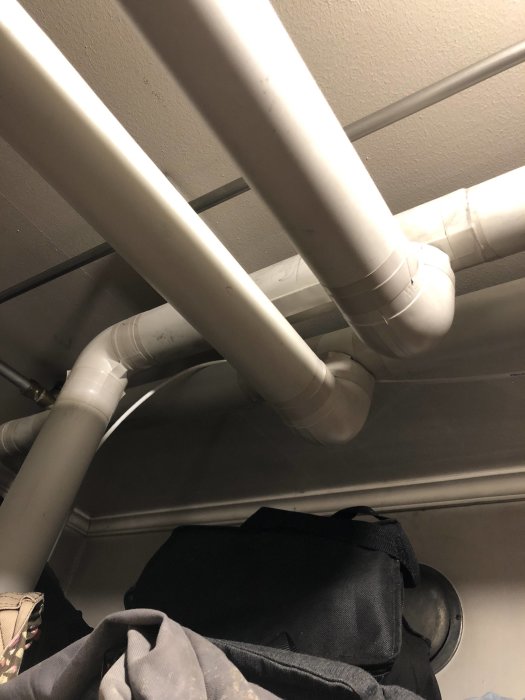 Vit VVS-rörinstallation med T-kopplingar och kläder i förgrunden.