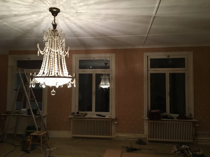 Renoveringsarbete i rum med tänd kristallkrona, stege, och verktyg på golvet.