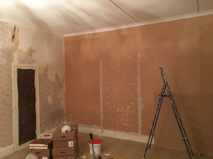Renovering av rum med delvis borttagen tapet, spacklade väggar och en stege.