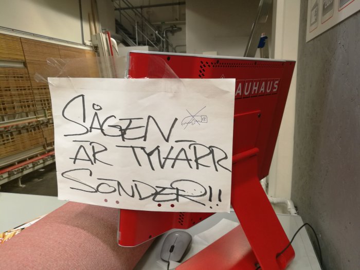 En röd sågstation med en handskriven lapp "Sågen är tvärr sönder!!" fäst på framsidan.
