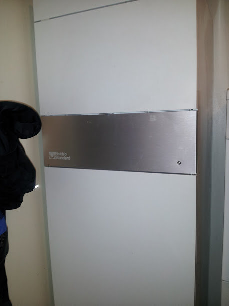 Äldre Aquaes 350 frånluftsvärmepump med synlig logotyp monterad på vägg, delvis dold av en person.