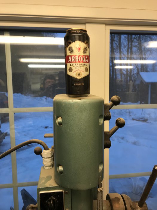 En ölburk placerad på toppen av en pelarborr framför ett fönster med utsikt över en snöig utomhusmiljö.