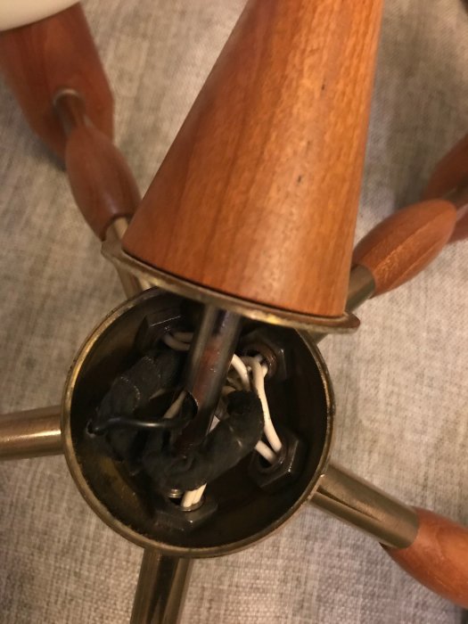 Inuti en öppen ljuskrona med två vita elkablar och svart tejp vid kopplingen.