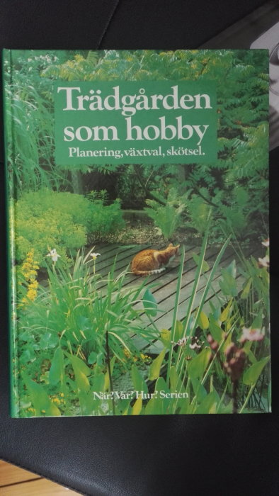 Bokomslag "Trädgården som hobby" med text om planering och växtval, katt sittande på trädäck omgiven av grönska.