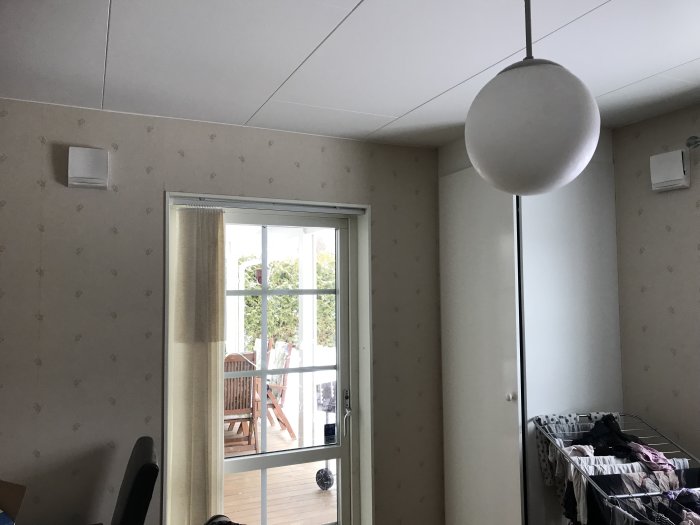 Interiör med uteluftsventiler, fönsterdörr till altan och en taklampa.