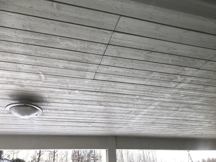 Vitmålat vindskydd under altantak med inbyggd belysningsarmatur, synliga trästrukturer, fråga gällande isolering.