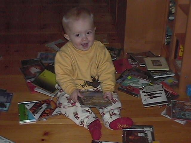 Leende bebis på furugolv omgiven av utspridda CD-fall.