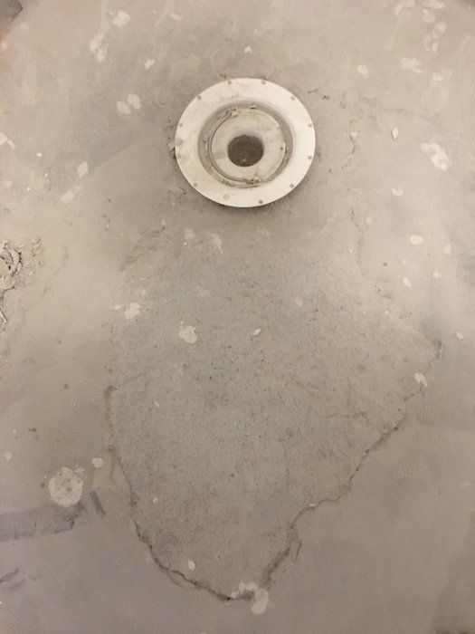 Badrumsgolv under renovering med avlopp och ojämnt applicerat flytspackel som inte ansluter till betongen.