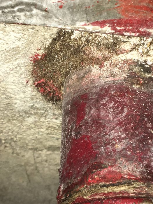 Brunt och trådigt isoleringsmaterial runt gammalt rör, eventuell asbest, behov av sanering.