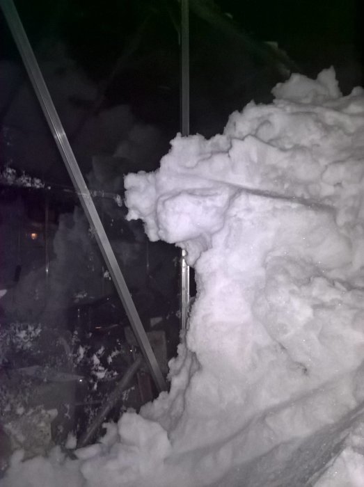 Växthus delvis täckt av snö i kvällsljus, som syns genom snöhög och strukturer.