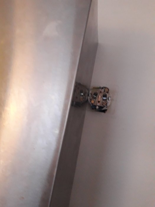 Eluttag placerat för nära en köksfläkts kåpa på en vit vägg, potentiell installationsutmaning.