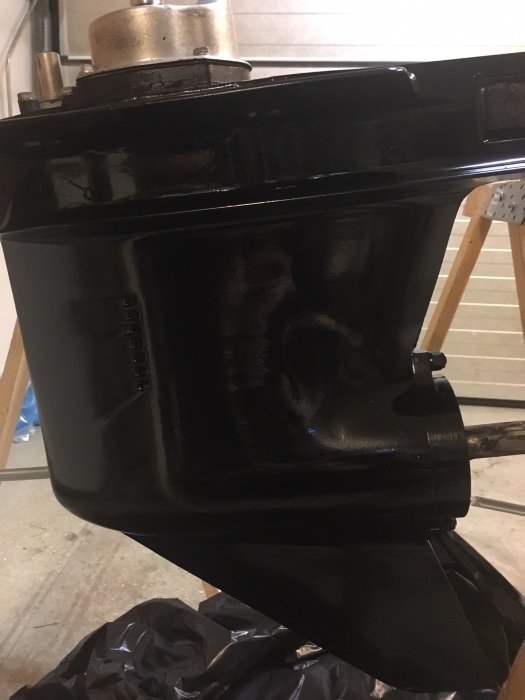 Nyligen omlackerad svart utombordare som står på ett golv med plastskydd under.