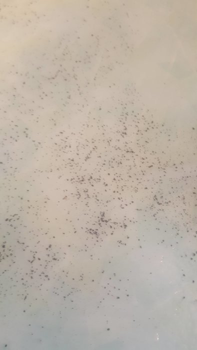 Svarta manganutfällningar på en vit yta, ger intryck av oljig konsistens.