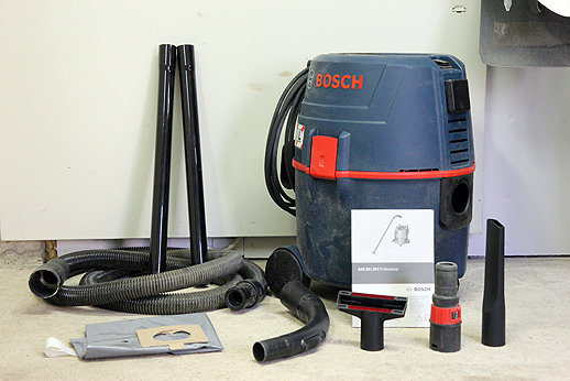 Bosch-dammsugare med grundkit av slangar och munstycken på ett betonggolv.