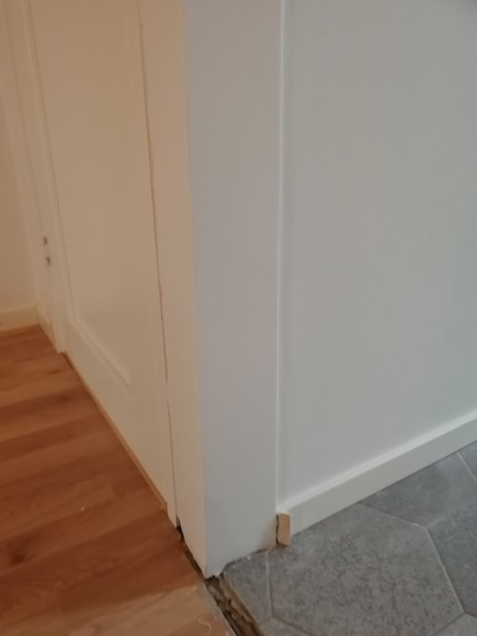 Nyligen spacklad och målad vägg och dörrkarm i ett hem, med synlig golvövergång från trä till kakel.