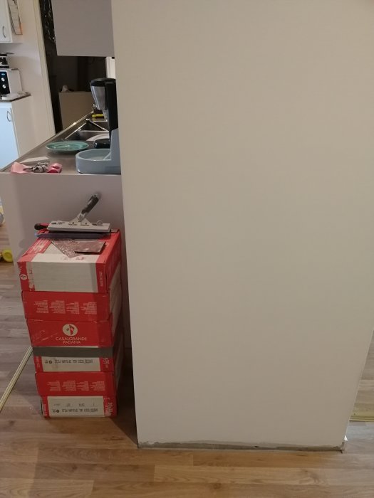 Nymålad och spacklad vägg bredvid röda kakellådor och verktyg vid köksentrén.