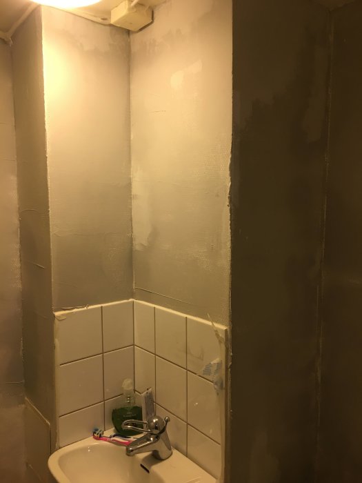 Ett badrum med väggar delvis täckta av nylagt och slipat spackel ovanför kaklade delar.