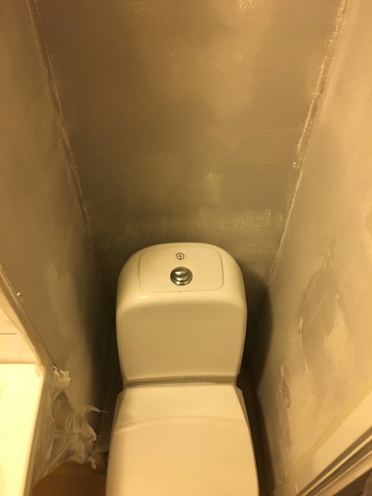 Toalett med nyligen spacklade och slipade väggar i ett badrum under renovering.