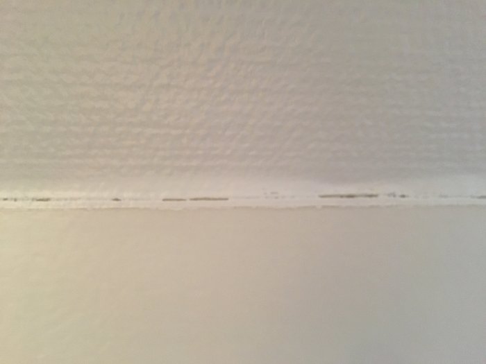 Sprucken fogmassa i skarv mellan vitmålad vägg och tak.