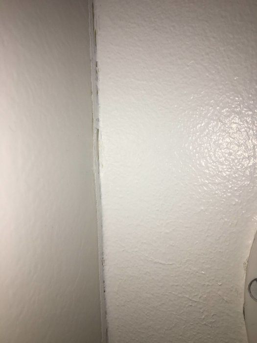 Sprucken fogmassa i skarven mellan en vit vägg och tak.