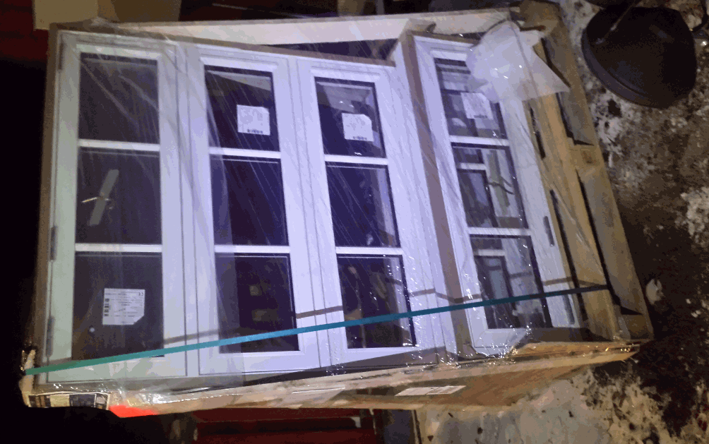 Oinbyggda vita spröjsade fönster med aluminiumlist, liggande på en pall skyddade av plast.