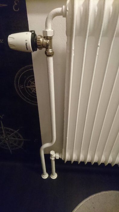 Vit radiator med termostat och nedåtgående rör mot golvet, eventuellt med returventil.