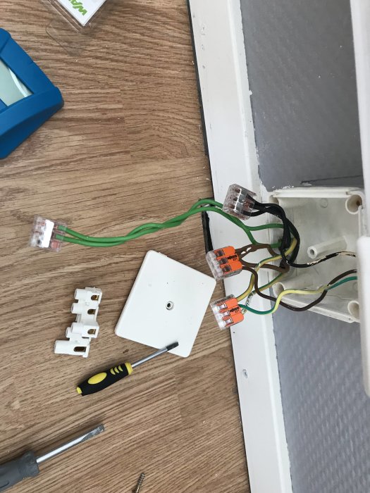 Öppen kopplingsdosa med borttagen plint, installerade wago-kopplingar och gröna kablar på trägolv.