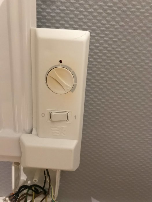 Termostat på vägg med öppen kåpa som exponerar ledningar, vred i mittenläge, till/från-switch under.