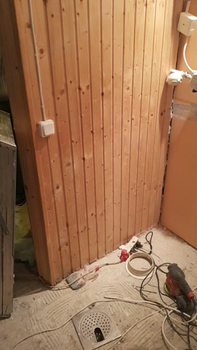 Renoveringsarbete med träväggar och golvbrunn, verktyg och kablar på golvet.