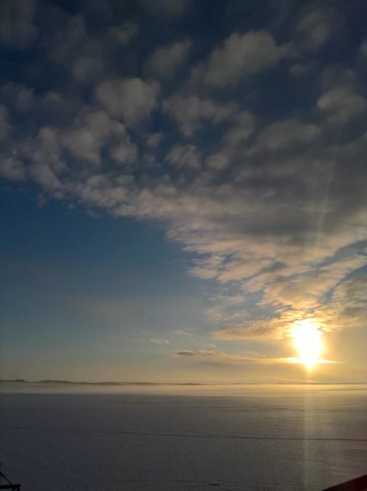 Vintersoluppgång över ett fruset landskap med dis på ytan och molnigt himmel.