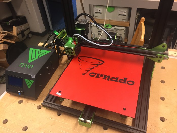 3D-skrivare med gröna komponenter och röd byggplatta, märkt med "Tornado", i verkstadsmiljö.