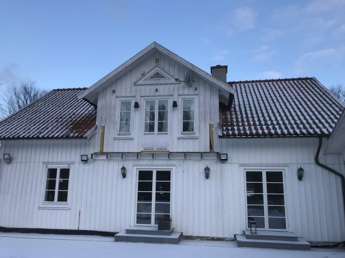 Vitt trähus med snötäckt mark och detalj från sidan inför planerad balkongbyggnation.