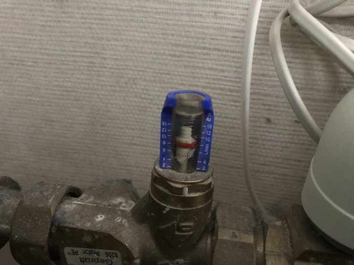 En blå vattenflödesmätare på rör med avläsning på 0 liter per minut i en tvättstuga.