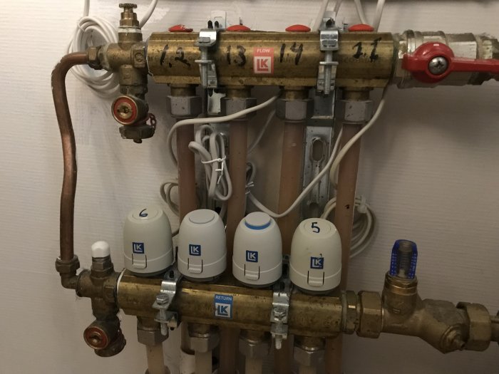 Installationsvy av golvvärmeställdon och rör med flödesmätare i en tvättstuga.