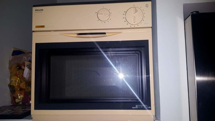 En gammal beige Philips mikrovågsugn inbyggd i ett mörkt köksskåp.
