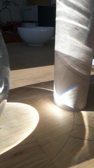 Solreflektion på köksgolvet med en vit skål i bakgrunden och en del av ett glas i framkant.