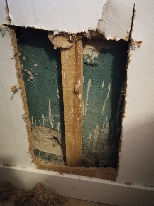 Öppning i vägg som avslöjar träreglar och skadad, fuktig puts.