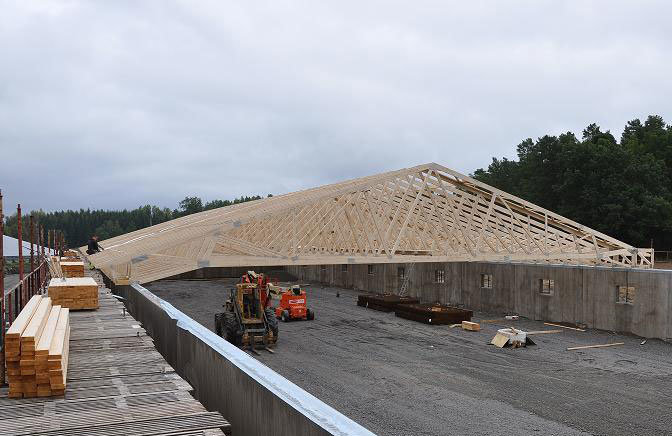 Stor W-takstol av konstruktionsvirke på byggarbetsplats under grå himmel.