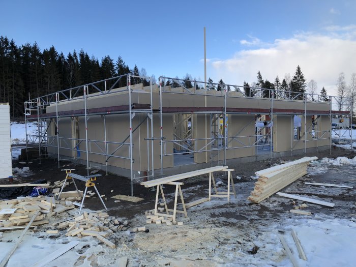 Garagebygge med ställningar uppställda, GU-gips monterat och byggmaterial på marken.