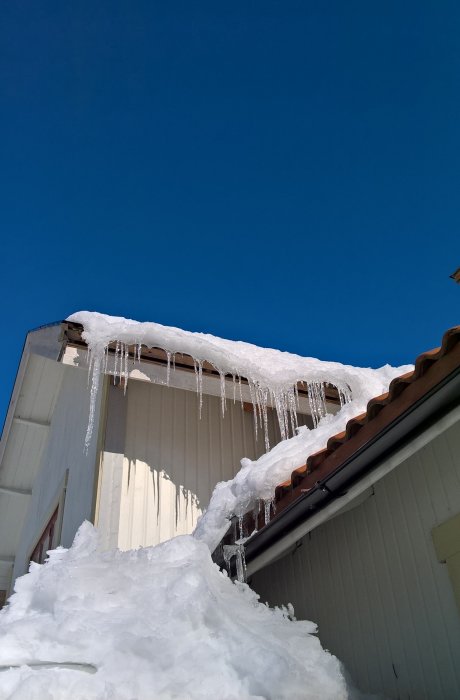 Altan täckt av snö med istappar hängande från taket mot en klarblå himmel.