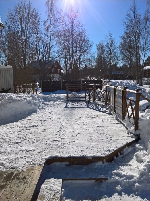 Delvis skottad altan med snöhögar runtomkring, trägeländer och soligt vinterväder i bakgrunden.