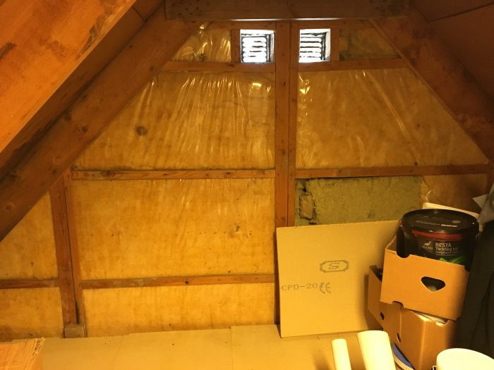 Isolerad vindsvåning med plastfolie och exponerade träbjälkar plus fönsterventiler.